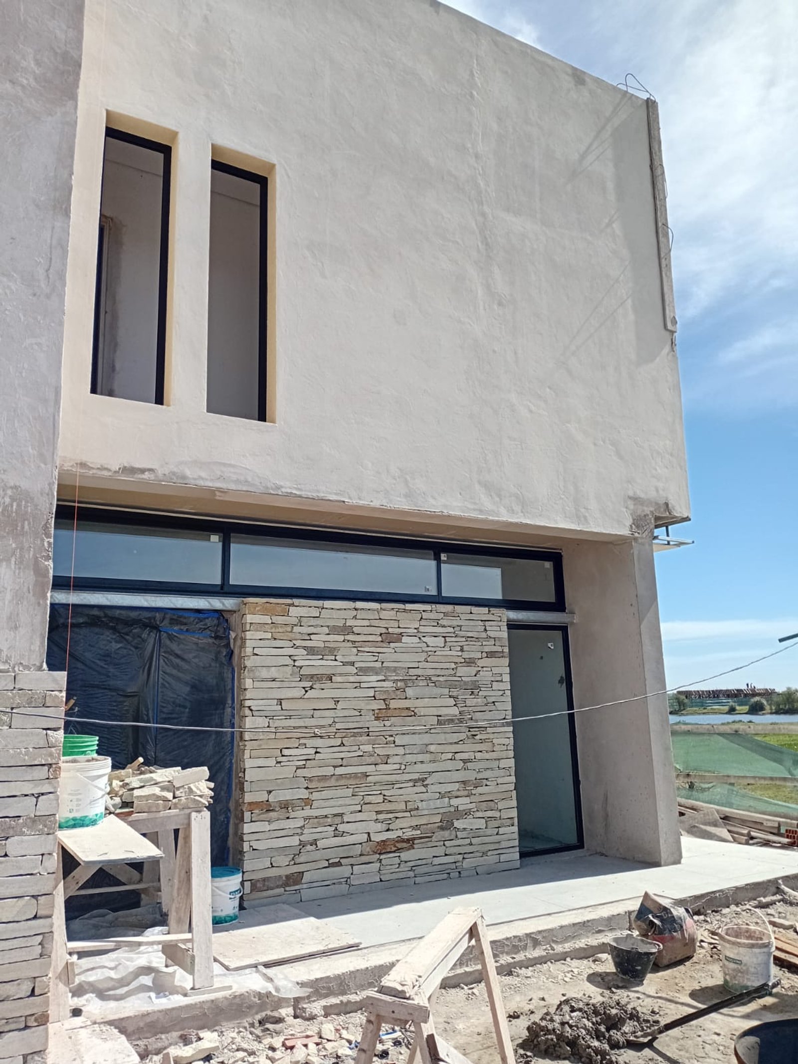 Fachada de casa moderna em construção com revestimento de pedra — projeto Casa en Pueblos del Plata, por Arquitecto Guido Niccoli, em Guillermo Enrique Hudson